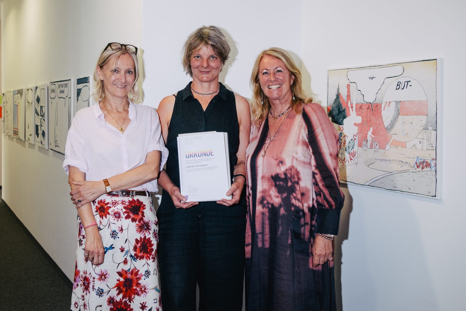 Gabriele Horndasch mit der Urkunde des FBZ art award 2025, links Silvia Schneider, rechts Tanja Quadflieg, daneben Arbeiten aus der Serie Sigh. Seufz. Ouf.